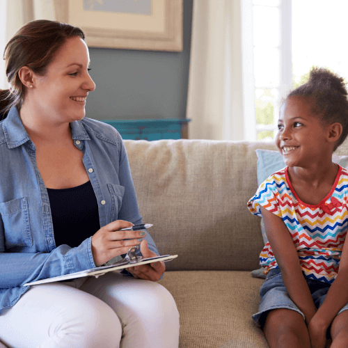 A smiling child looking at a smiling adult who is holding a clipboard and a pen