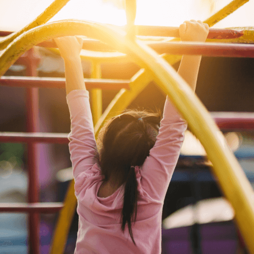 A child holding onto yellow and red monkey bars