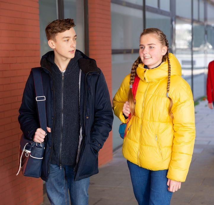 two students carrying bags walking and talking on the street